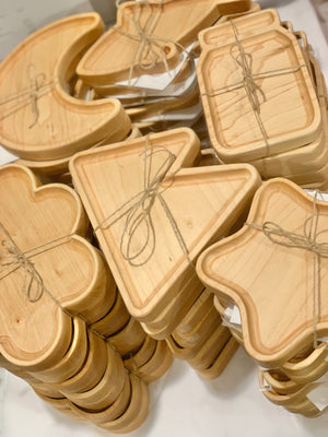 Stacked wooden sensory trays in various shapes including moon, clover, triangle, and jar tied with twine on white surface