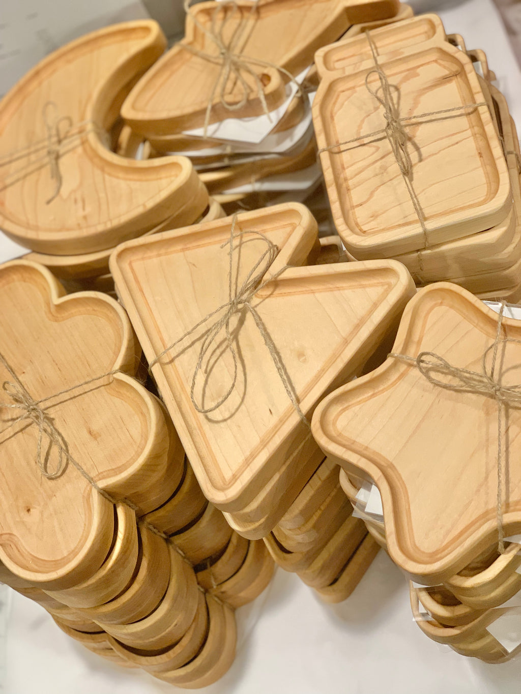 Stacked wooden sensory trays in various shapes including moon, clover, triangle, and jar tied with twine on white surface