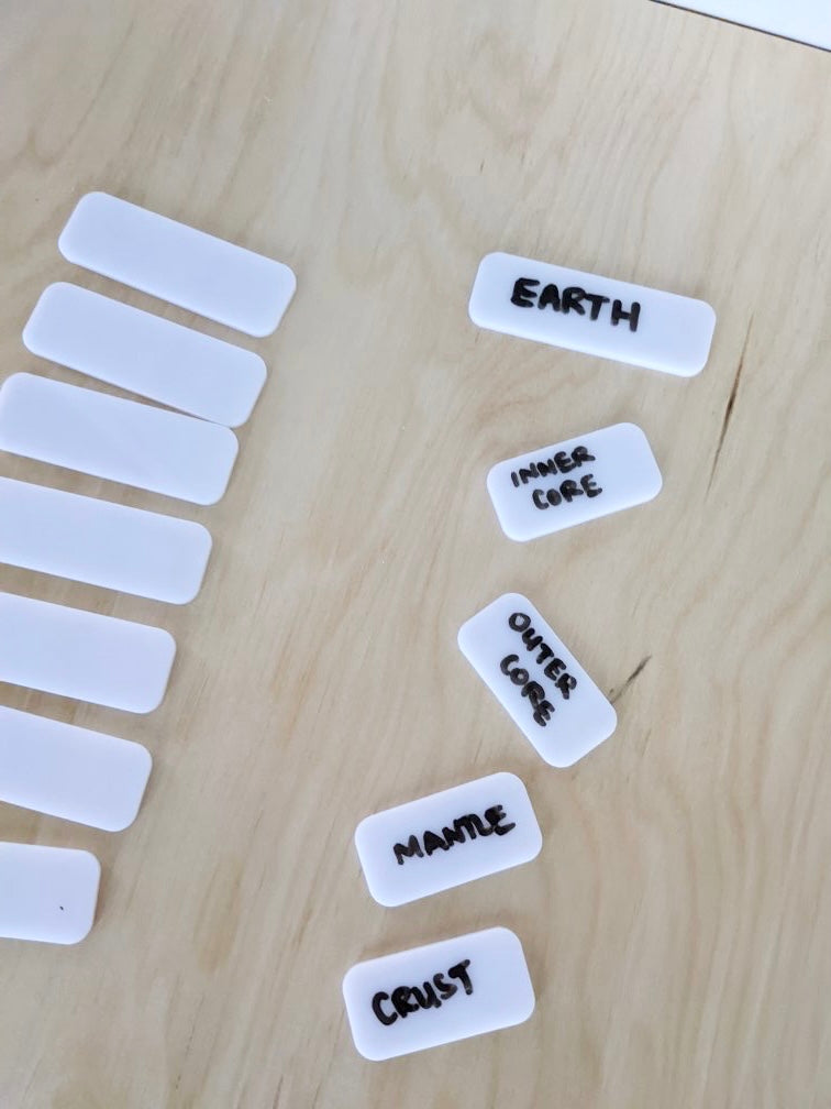 16 white rectangular dry erase placards, some blank and some labeled with Earth layers on light wood surface