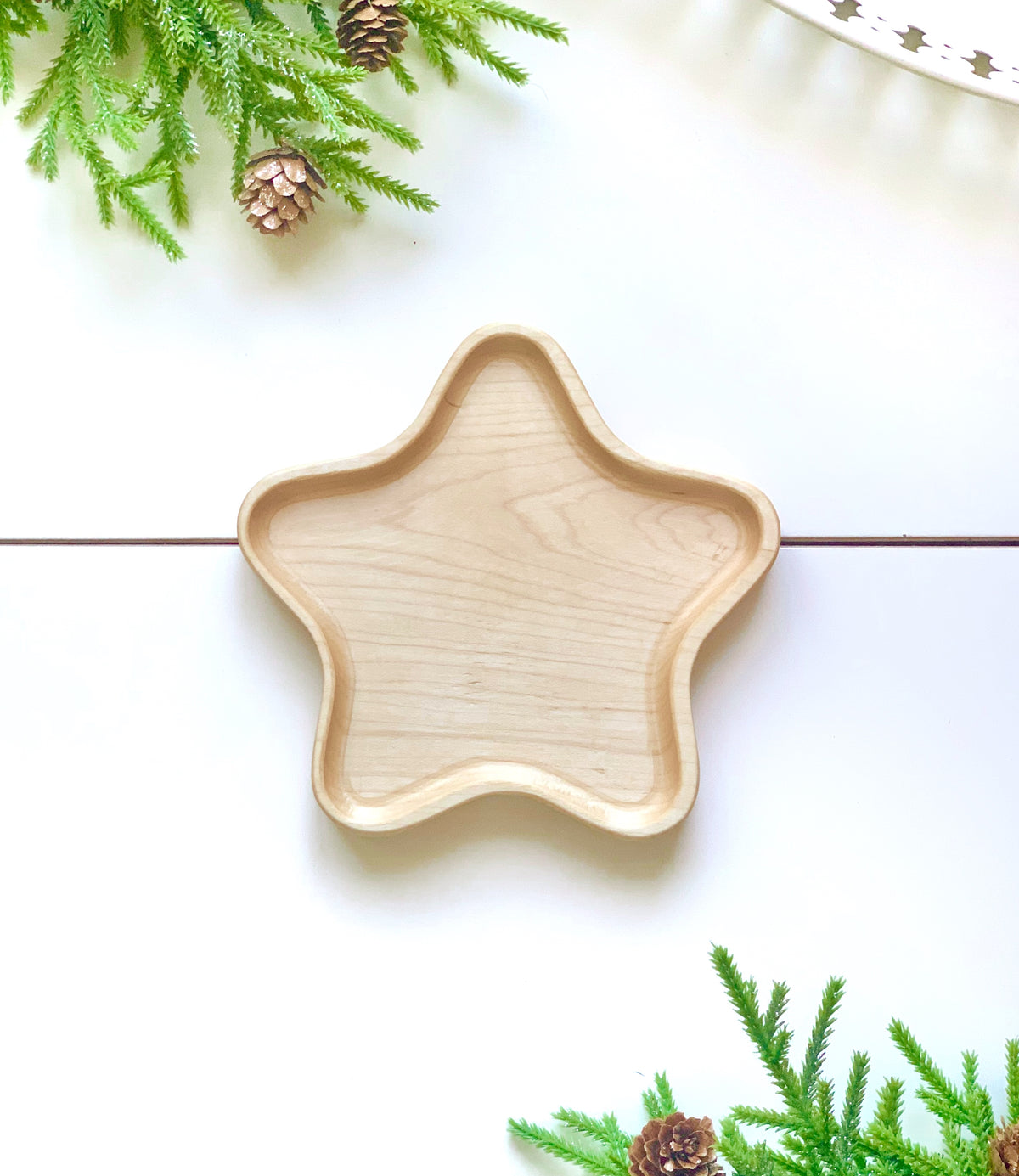 Natural wooden star-shaped sensory tray on white surface with green pine branches and pinecones around edges