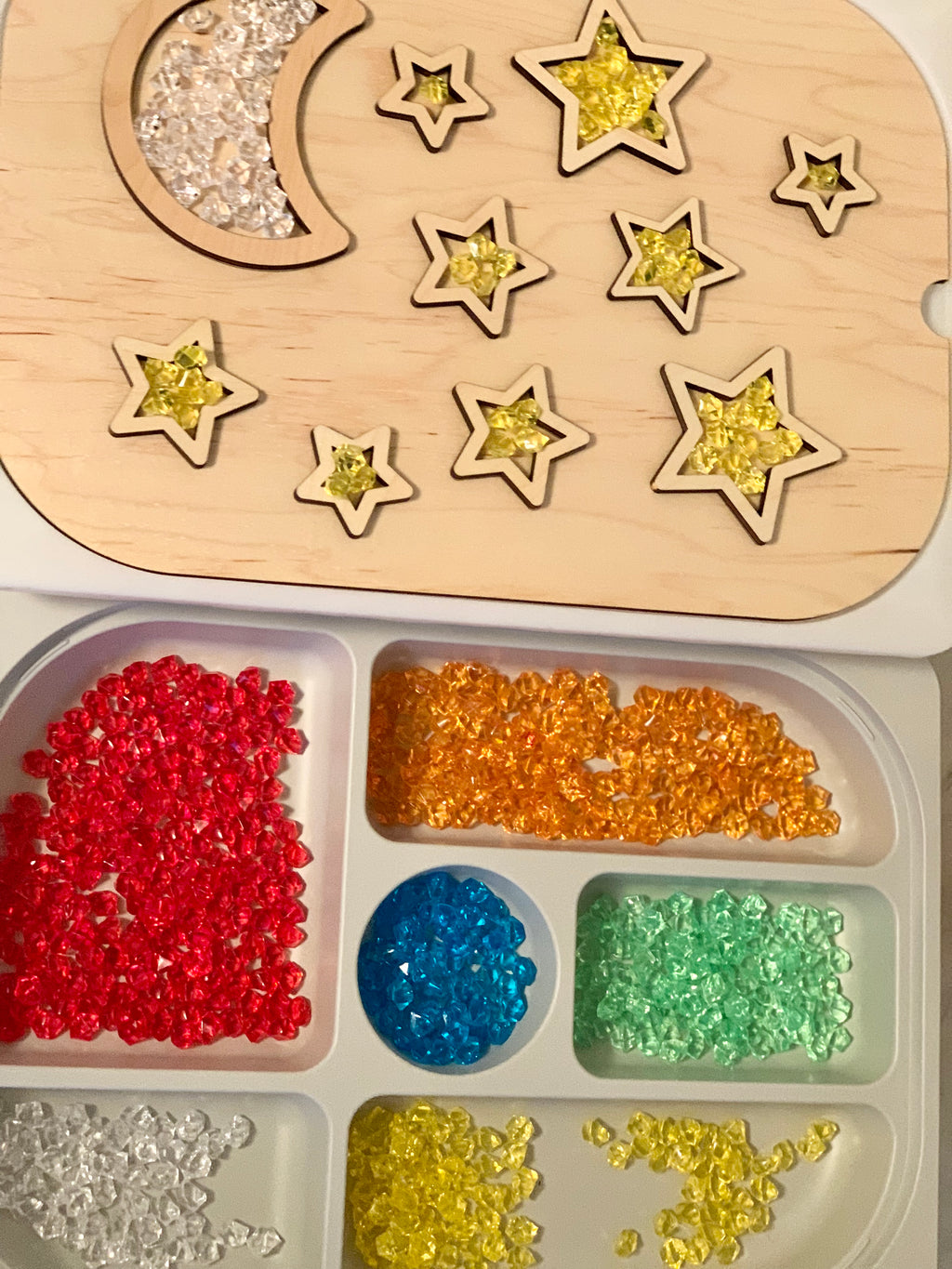 Maple wood night sky insert with moon and star shapes filled with yellow and clear translucent beads on white tray with colorful gems