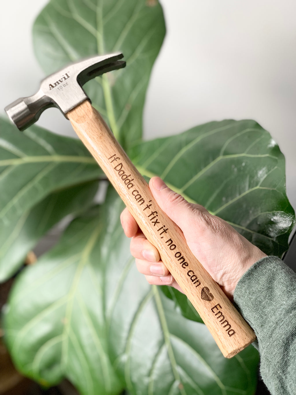 Personalized wooden hammer with laser engraved custom message held by hand against green leaf background