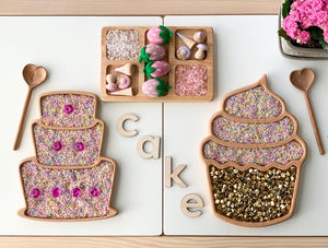 Wooden cupcake and cupcake-shaped sensory trays filled with colorful dried flowers and gold beads on white surface