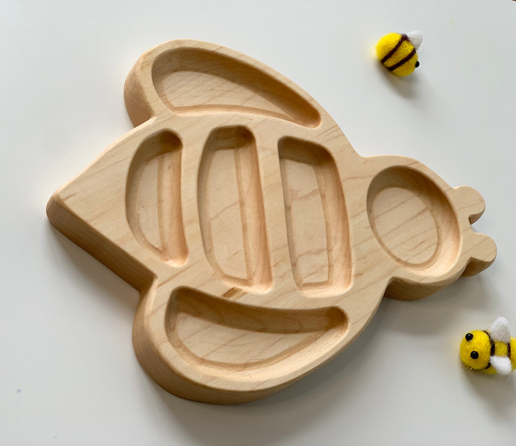 Natural wooden sensory tray shaped like a bee with carved sections on white background with two small plush bees
