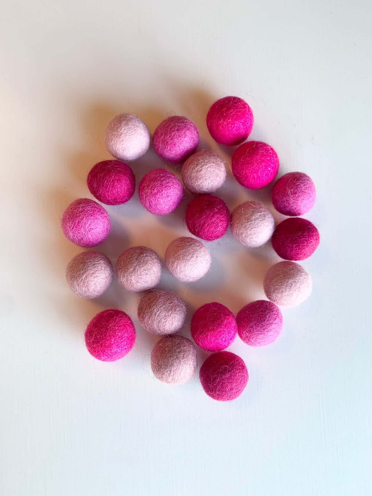 Assortment of pink felt balls in varying shades arranged on a white surface for sensory and craft use