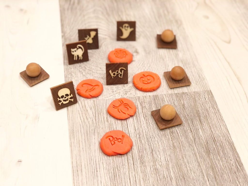 Small wooden Halloween play dough stamps with pumpkin, ghost, cat, and skull designs on light wood surface