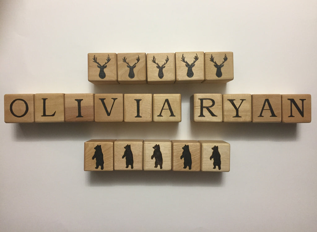 Natural wooden 1.5 inch custom blocks with black engraved letters spelling OLIVIA RYAN and animal silhouettes on white background