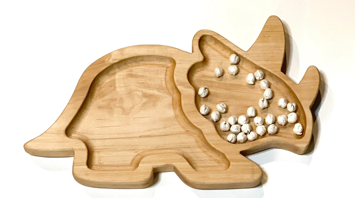 Natural wooden Triceratops-shaped plate with smooth carved compartments on white background with small white beads