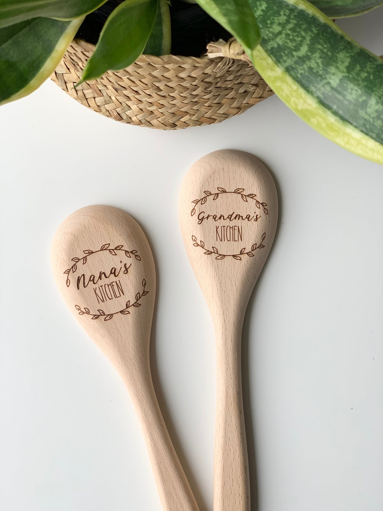Two personalized wooden spoons engraved with "Nana's Kitchen" and "Grandma's Kitchen" on light wood background
