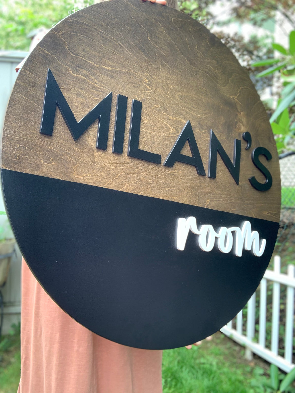 Round half painted wooden name sign with black and white 3D letters reading Milan’s room outdoors