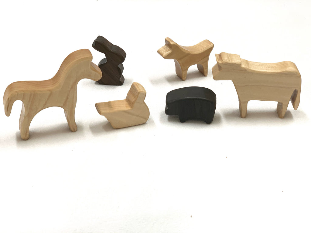 Set of six small natural and dark wood farm animal toy figurines on white background