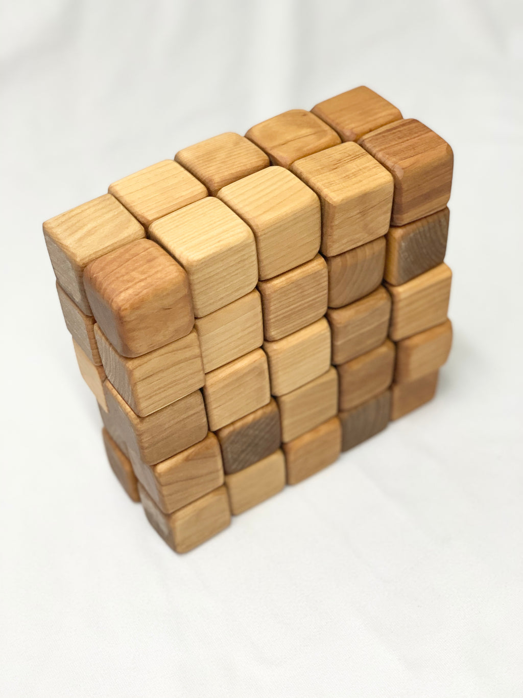 Natural unfinished 2-inch wooden blocks stacked in a grid pattern showing varied wood tones on white fabric background