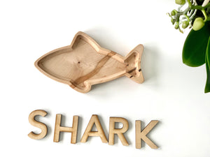 Natural wooden shark-shaped sensory plate with smooth finish on white background near green plant stem
