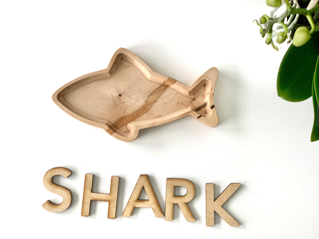 Natural wooden shark-shaped sensory plate with smooth finish on white background near green plant stem