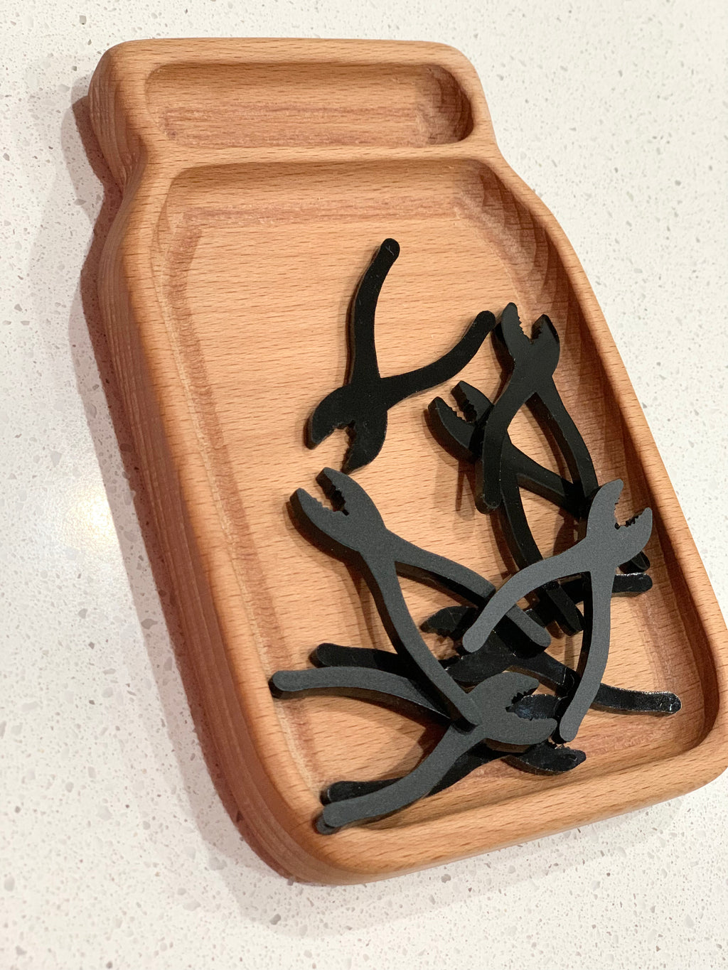 Wooden jar-shaped tray holding black acrylic tool shapes including pliers for sensory loose parts play on white surface
