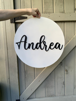 Hand holding 3D round white nursery sign with black cursive name Andrea on rustic wooden background