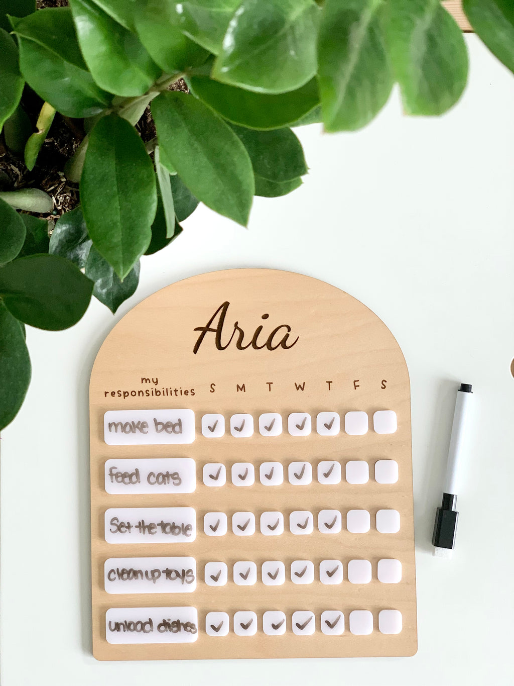 Personalized wooden chore chart with white acrylic dry erase tiles and black dry erase marker on white surface