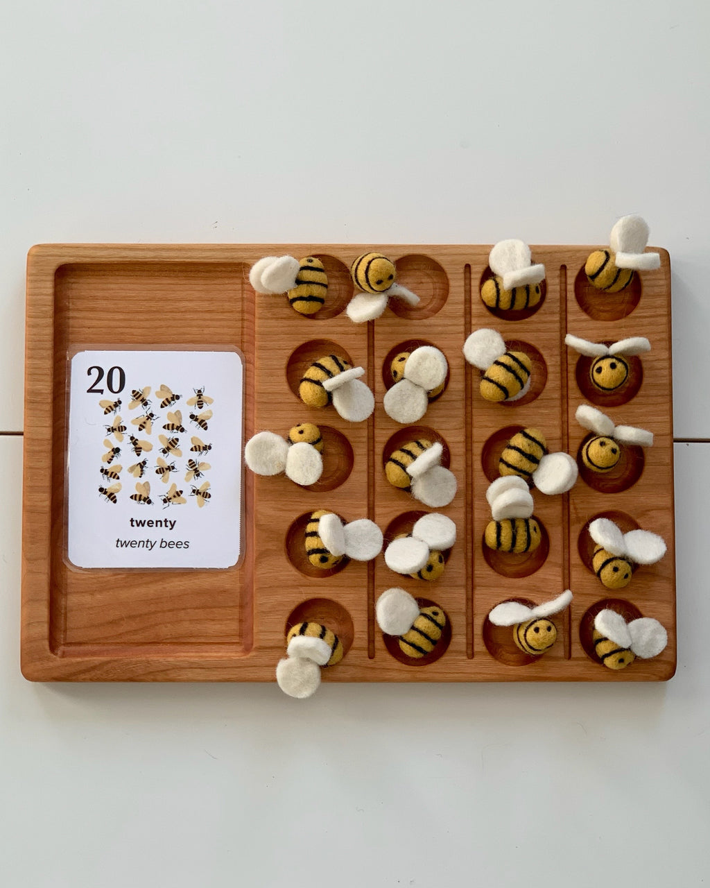 Wooden counting board with twenty felt bees featuring yellow and black stripes and white wings arranged in rows