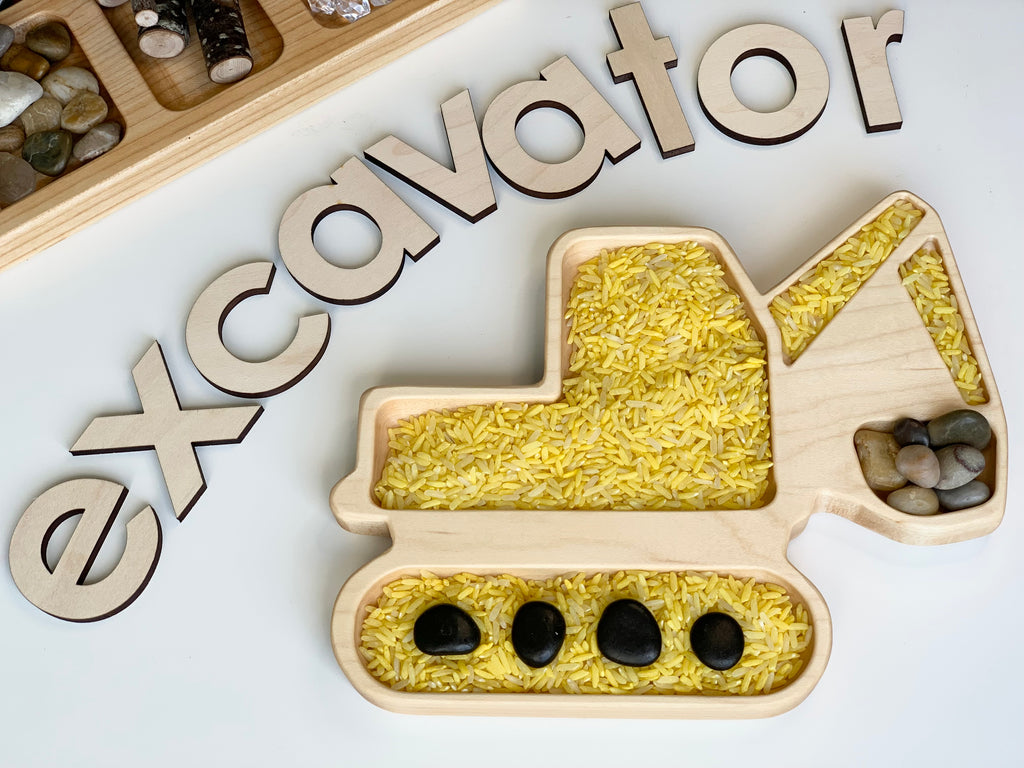 Wooden excavator-shaped sensory tray filled with yellow rice and black and brown stones on white background