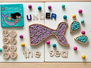 Mermaid tail sensory tray with purple and blue beads, wooden alphabet blocks spelling under the sea with sea creature stamps and felt balls