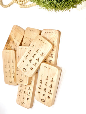 Natural wooden toy phones with engraved number pads arranged overlapping on white surface with green plant above