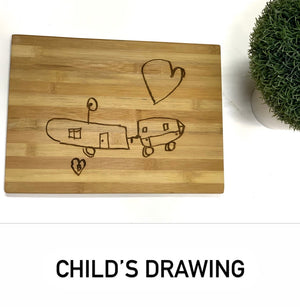 Personalized bamboo cutting board with child’s hand-drawn airplane and hearts engraved on natural wood surface