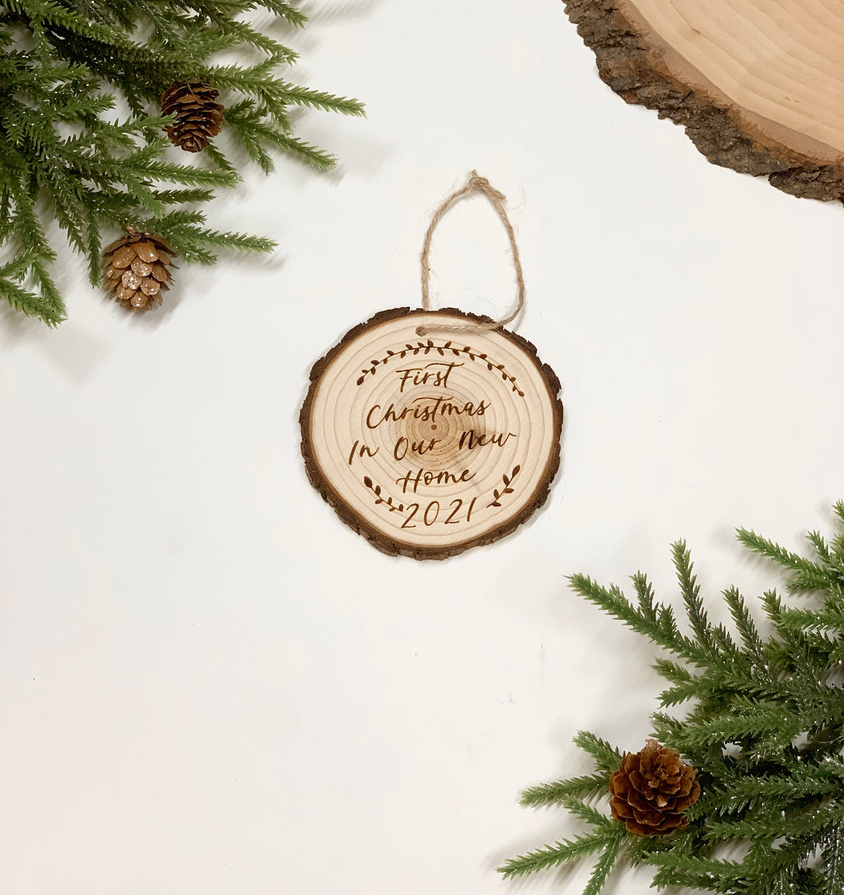 Round wood burned Christmas ornament with "First Christmas in Our New Home 2021" text and rustic twine hanger on white background