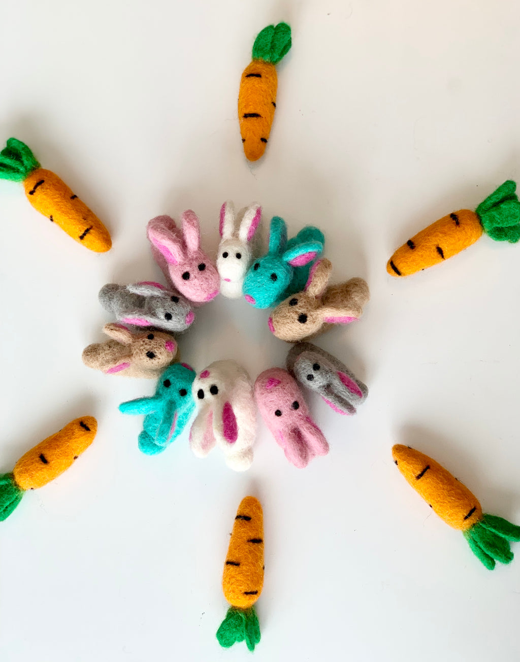 Circle of small colorful felt bunnies surrounded by handmade felt carrots on white background
