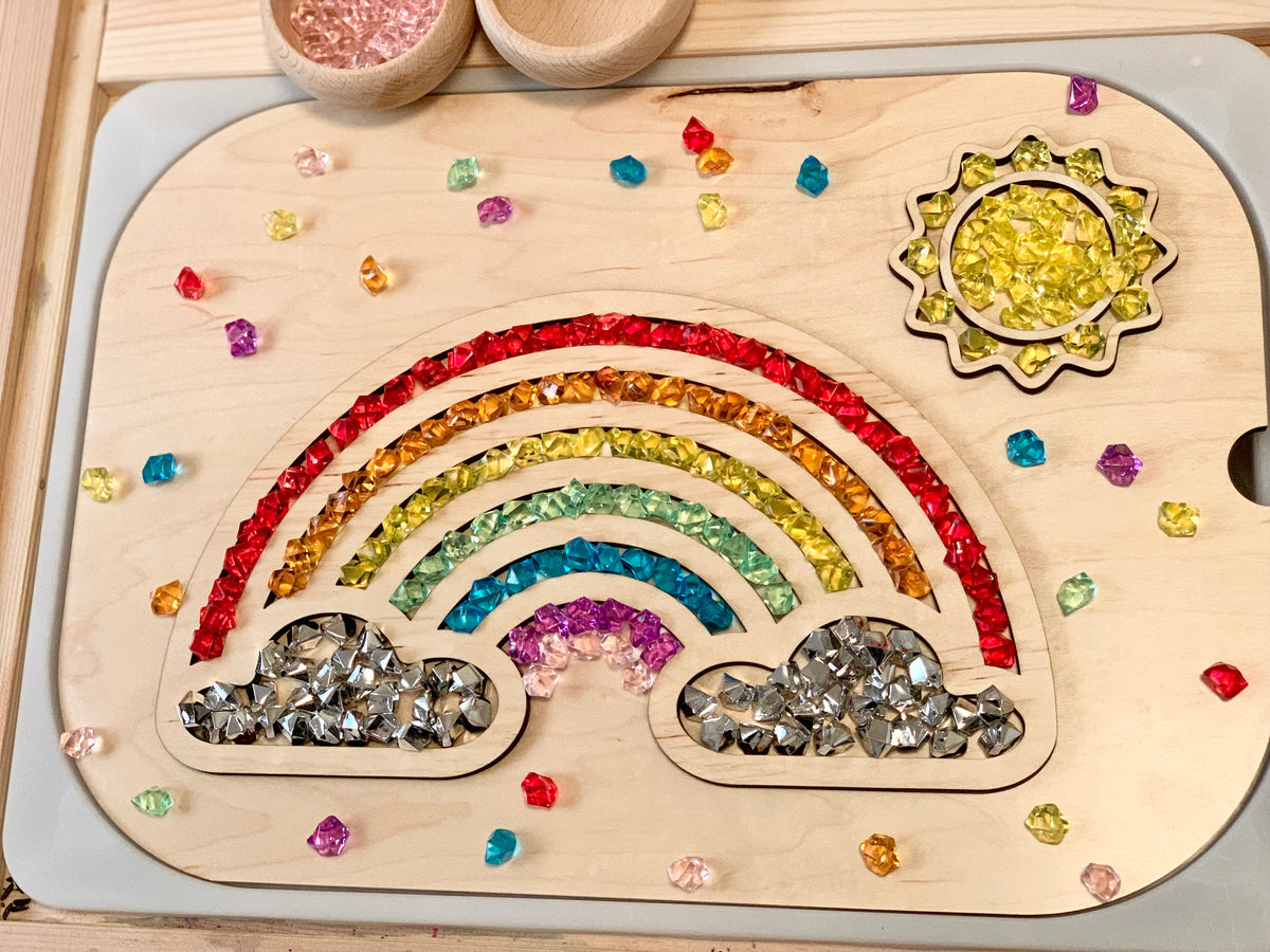 Wooden rainbow tabletop insert filled with colorful acrylic gems and a yellow sun shape on a light wooden surface