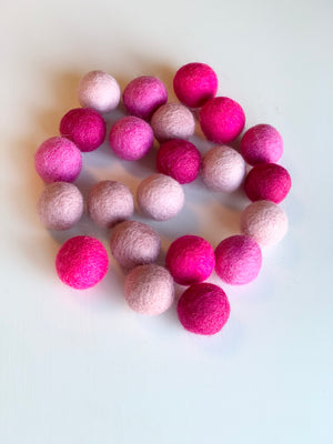 Assortment of pink felt balls in various shades arranged on a white surface in a loose circle