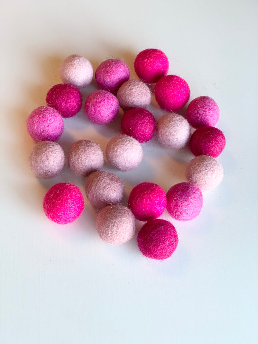 Assortment of pink felt balls in various shades arranged on a white surface in a loose circle