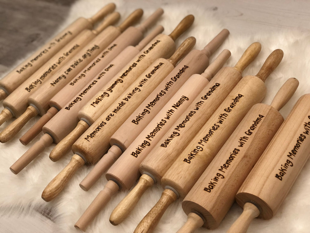 Assorted personalized wooden rolling pins with custom wood burned messages on smooth wood surface arranged on soft fabric