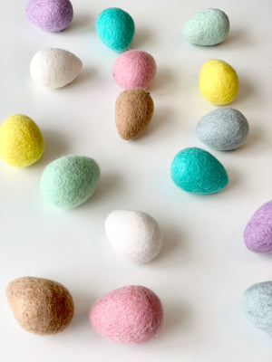 Assorted colorful handmade felt Easter eggs in pastel shades scattered on white surface