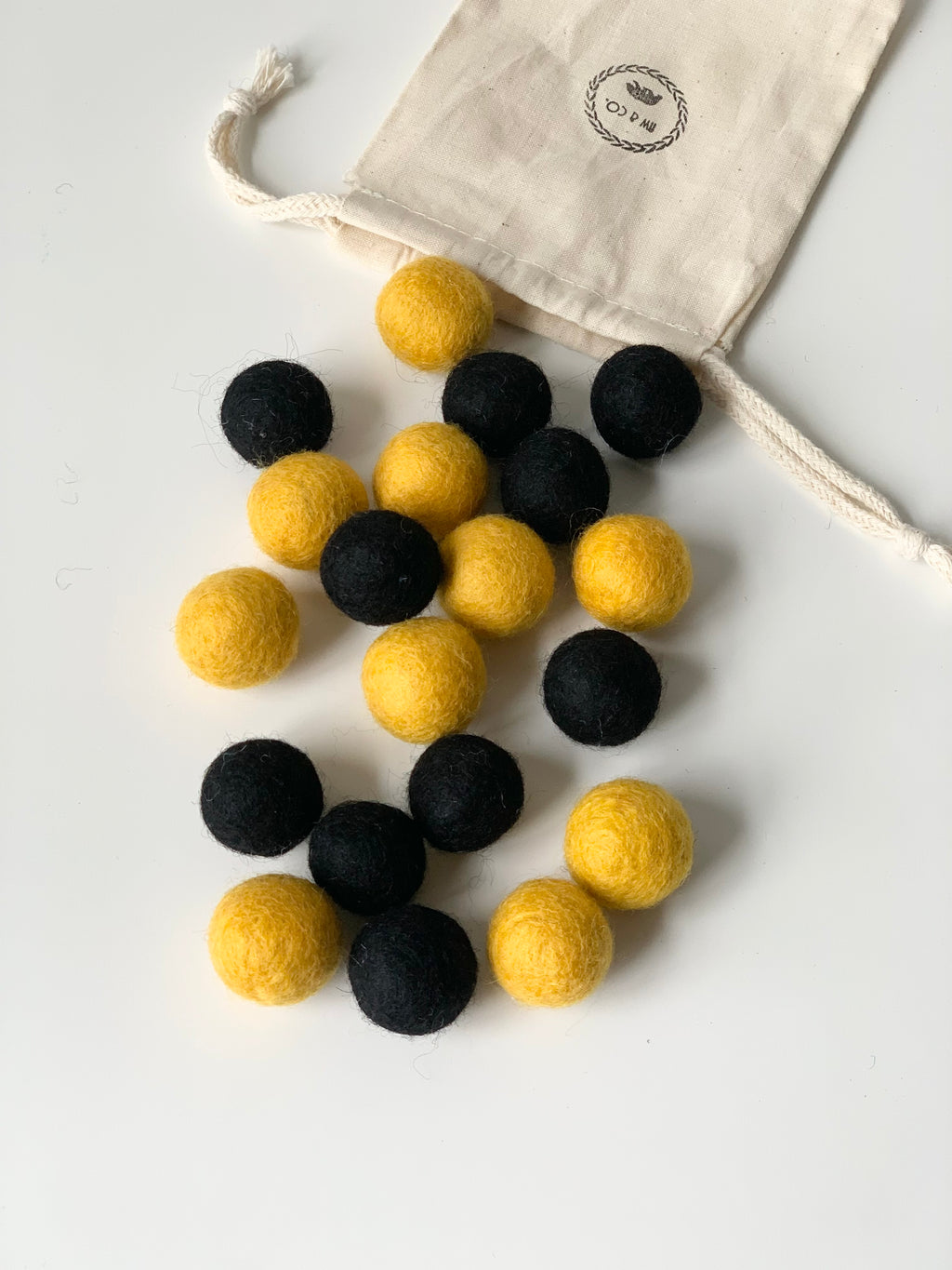 Yellow and black felt balls scattered on white surface with small natural drawstring fabric bag partially open