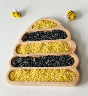 Bee Hive Plate sensory tray filled with alternating yellow and black rice grains with two small felt bees on white background