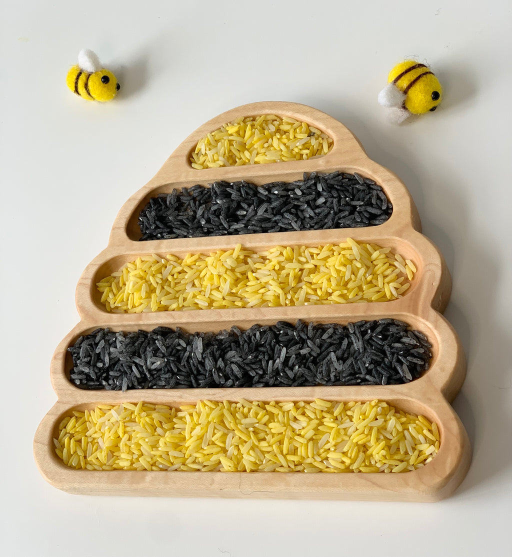 Bee Hive Plate sensory tray filled with alternating yellow and black rice grains with two small felt bees on white background