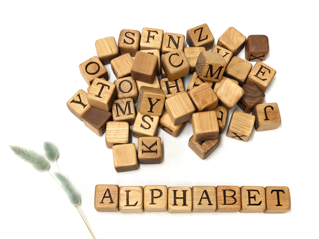 Natural 2-inch wooden alphabet blocks with engraved capital letters scattered and arranged to spell ALPHABET on white background