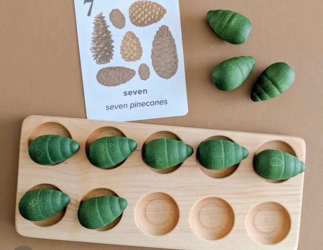 Natural wooden ten frame tray with eight green wooden pinecone counters and a counting card showing seven pinecones
