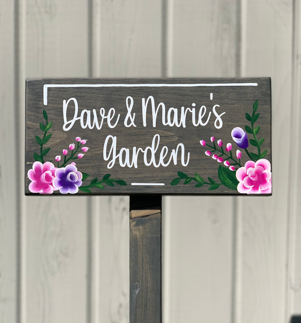 Large custom wooden garden sign with white cursive letters and pink and purple floral illustrations on dark wood background