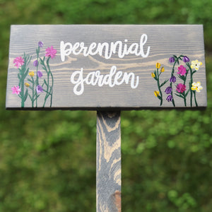 Custom wooden garden sign painted gray with white cursive letters and colorful floral illustrations on wood grain background