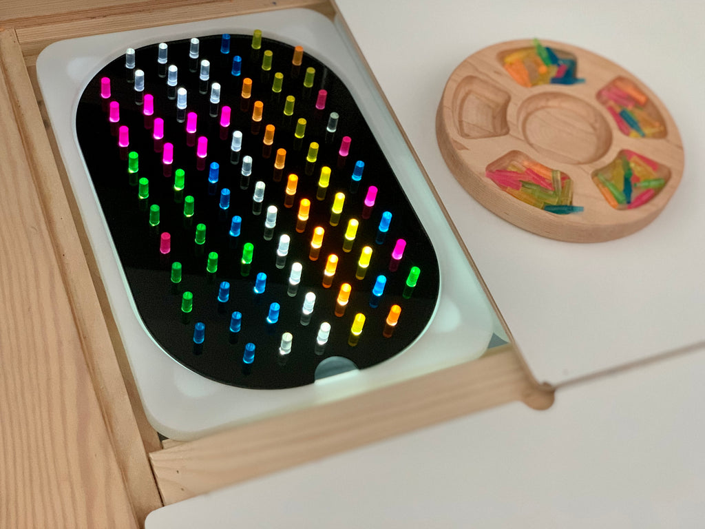 Small hole peg board add on with colorful translucent pegs in wooden geometric light board insert on wood table surface