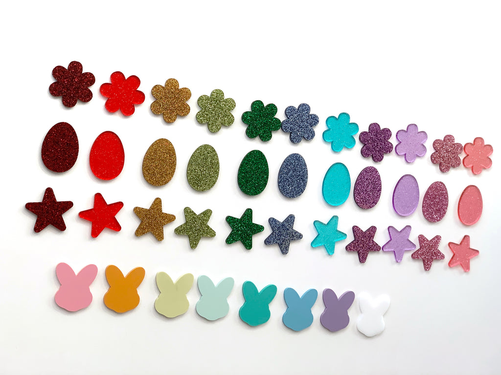 Rows of colorful laser cut acrylic shapes including flowers, eggs, stars, and bunny silhouettes on white background