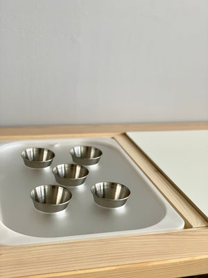 Set of five small metal cups arranged inside a wooden tray with white acrylic insert on light background