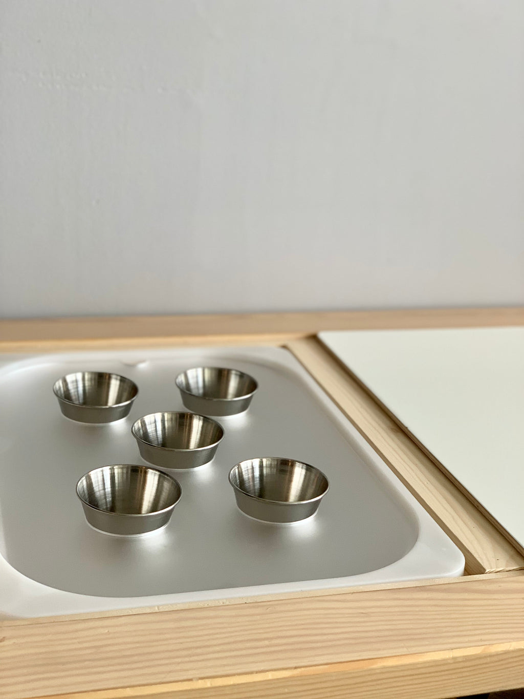 Set of five small metal cups arranged inside a wooden tray with white acrylic insert on light background