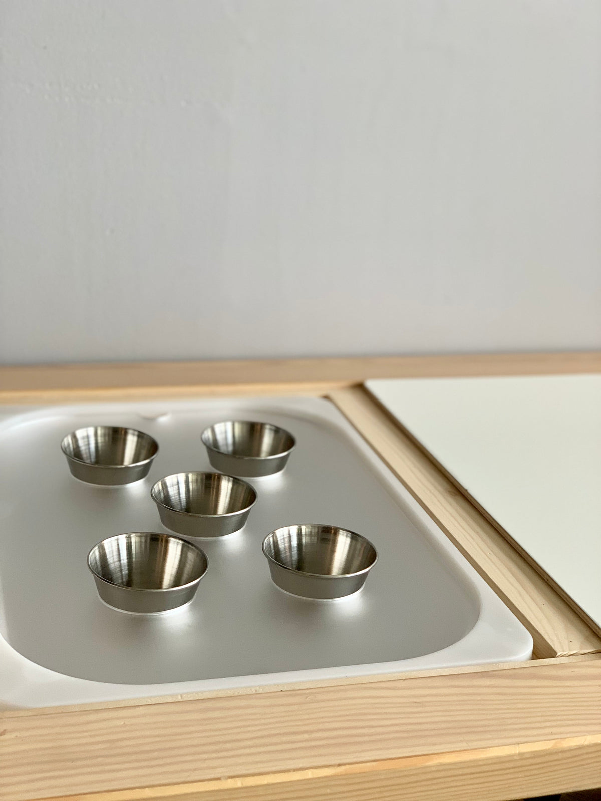 Set of five small metal cups arranged inside a wooden tray with white acrylic insert on light background