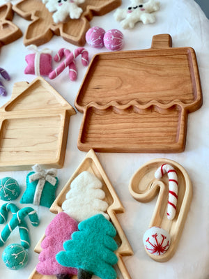 Natural wooden gingerbread house plate and tree tray with felt holiday decorations on white fabric background