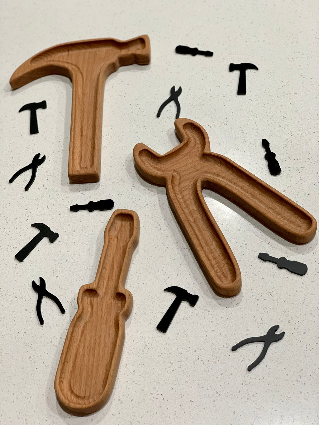 Wooden tool-shaped sensory trays in hammer, screwdriver, and pliers shapes with small black tool cutouts on white surface