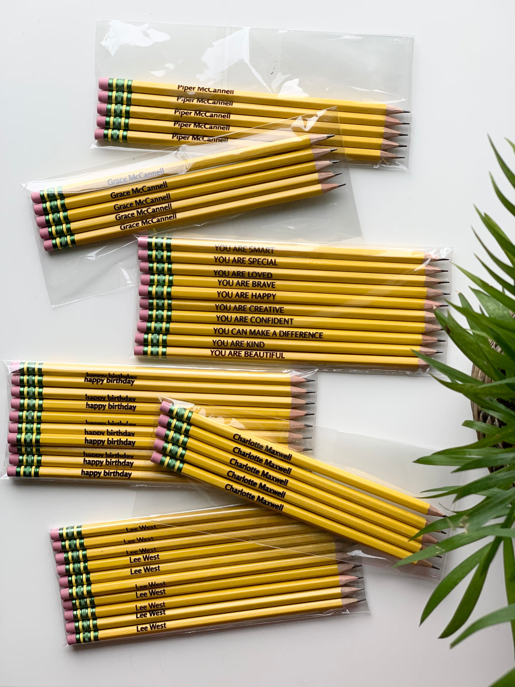 Bundles of personalized yellow Ticonderoga pencils with black custom names and motivational phrases in clear plastic packaging on white surface