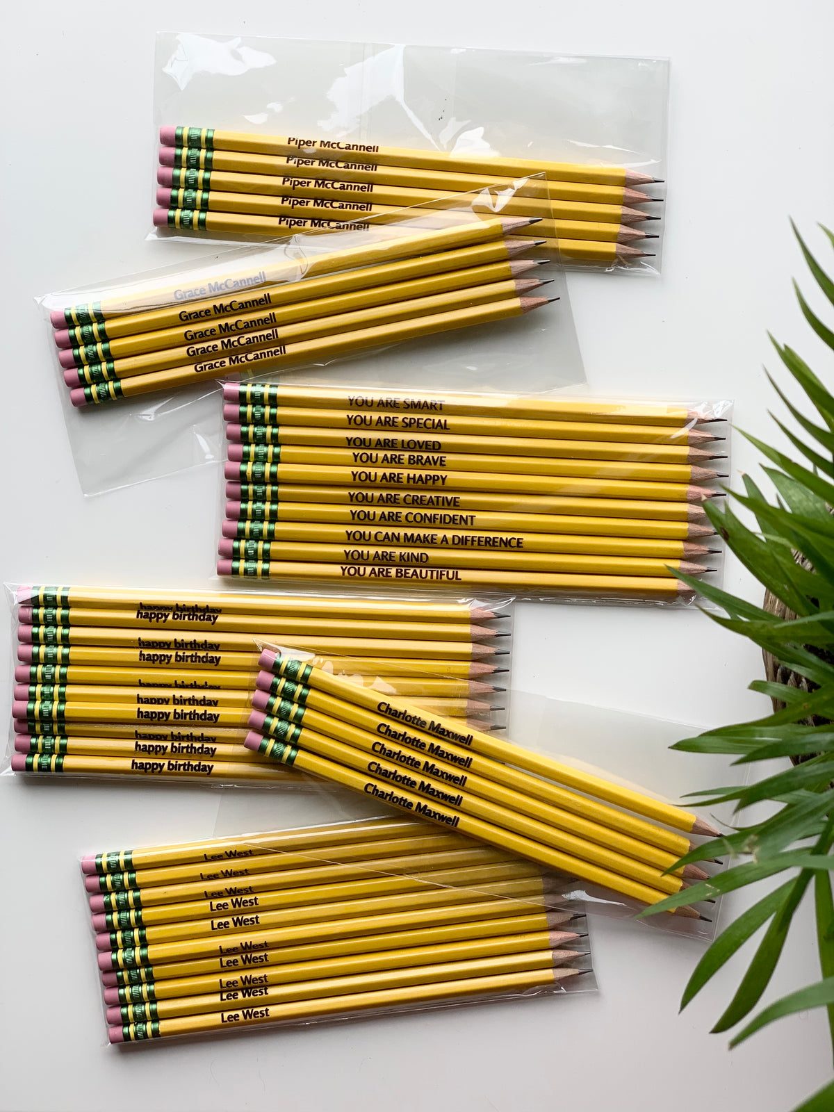 Bundles of personalized yellow Ticonderoga pencils with black custom names and motivational phrases in clear plastic packaging on white surface