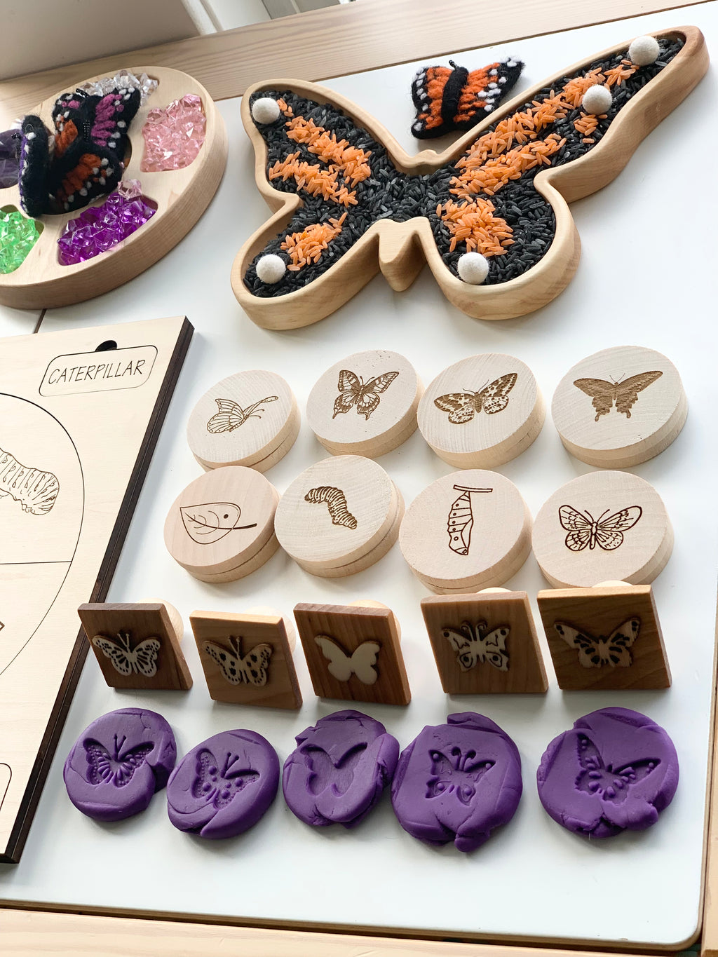 Wooden butterfly life cycle memory game pieces including discs, stamps, and butterfly-shaped tray with colored rice on white surface